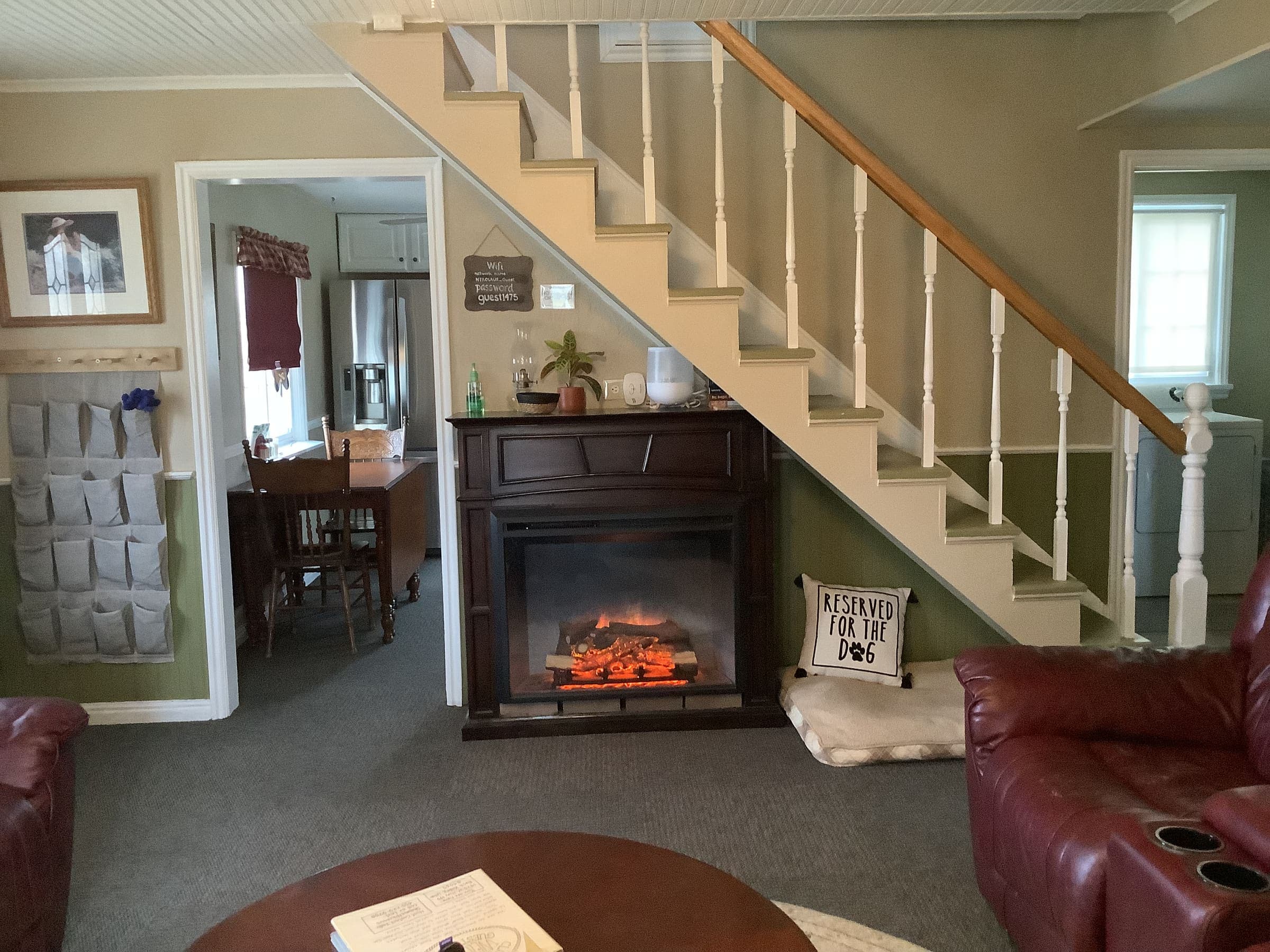 Front room of the farmhouse with an electric fireplace, maroon leather sofa, and staircase to the loft